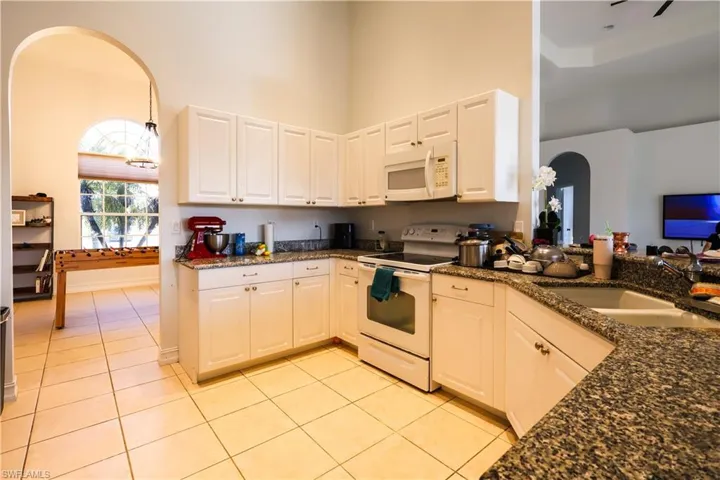 Kitchen with arched walkways, white appliances, dark stone countertops, white cabinets, and a high ceiling