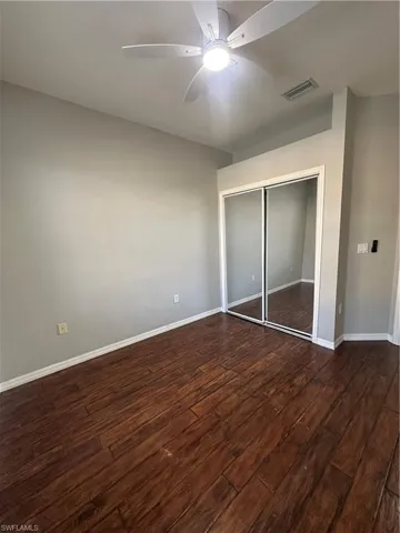 Unfurnished bedroom with a closet, dark wood-type flooring, and a ceiling fan