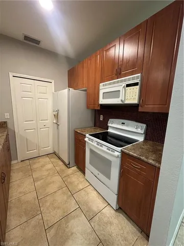 Kitchen with white appliances, backsplash, brown cabinetry, and light tile patterned flooring
