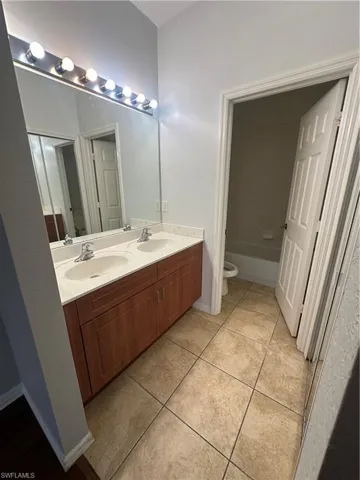Full bath featuring double vanity, light tile patterned floors, and washtub / shower combination