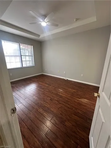 Empty room with a raised ceiling, dark wood-type flooring, and a ceiling fan
