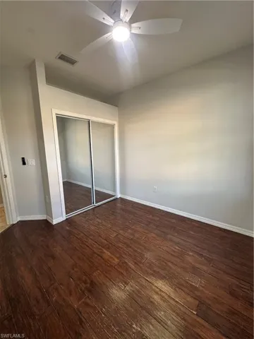 Unfurnished bedroom with a closet, dark wood-style flooring, and ceiling fan