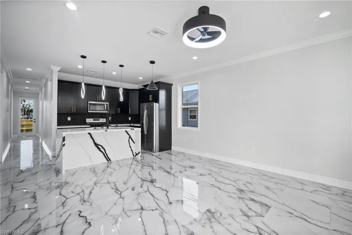 Kitchen with a kitchen island with sink, hanging light fixtures, crown molding, appliances with stainless steel finishes, and tasteful backsplash