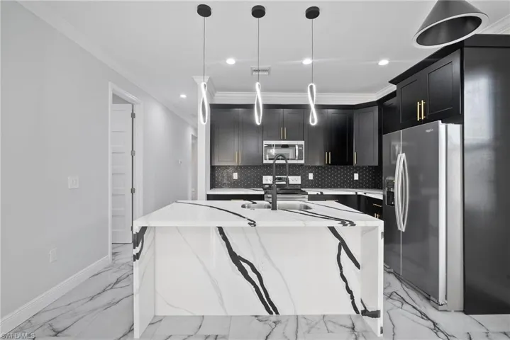 Kitchen featuring light stone countertops, appliances with stainless steel finishes, decorative light fixtures, and crown molding