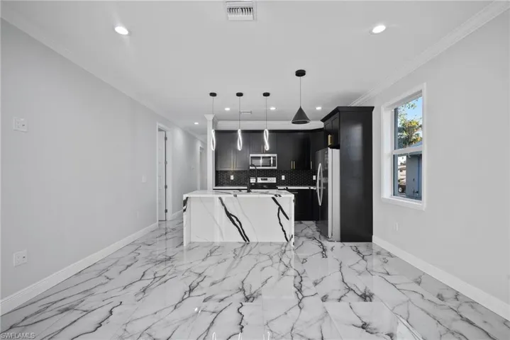 Kitchen with tasteful backsplash, crown molding, an island with sink, pendant lighting, and appliances with stainless steel finishes