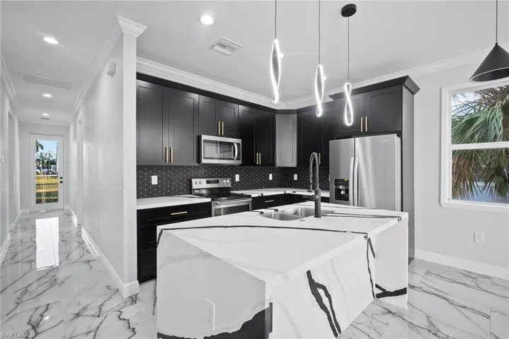 Kitchen with a healthy amount of sunlight, a kitchen island with sink, stainless steel appliances, and ornamental molding
