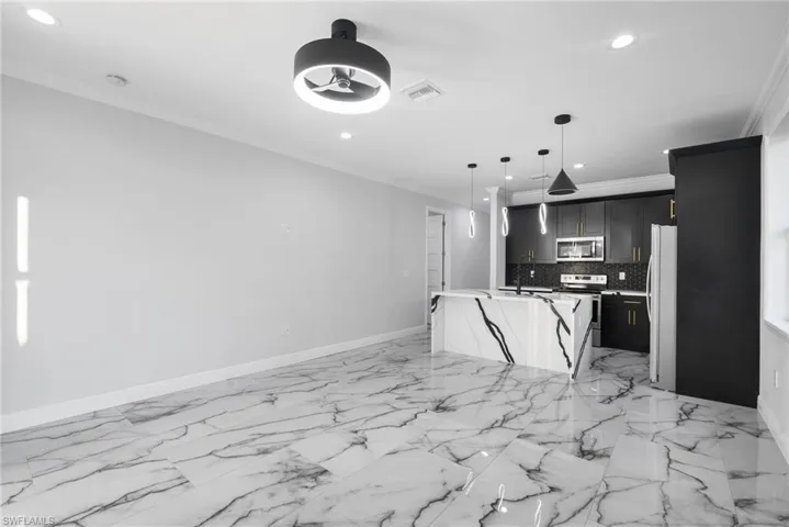 Kitchen with white refrigerator, backsplash, decorative light fixtures, a kitchen island with sink, and ornamental molding