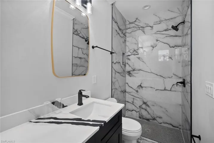 Bathroom featuring a tile shower, vanity, and toilet