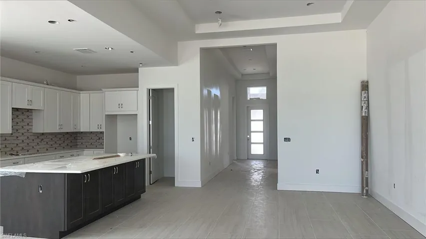 Kitchen with white cabinets, light stone counters, a raised ceiling, decorative backsplash, and cooktop