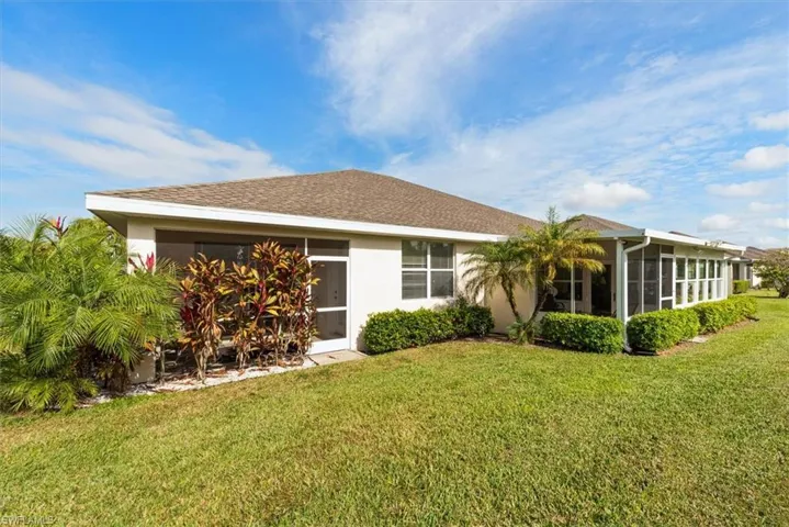 Back of property with a lawn, stucco siding, a shingled roof, and a sunroom