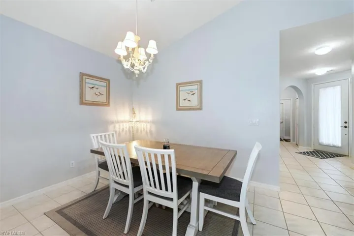 Dining room featuring light tile patterned floors, vaulted ceiling, and a chandelier
