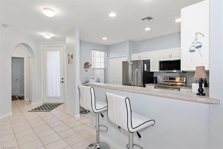 Kitchen featuring a breakfast bar, white cabinetry, appliances with stainless steel finishes, light countertops, and arched walkways