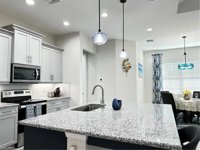 Kitchen with a breakfast bar, stainless steel appliances, light stone countertops, and a center island with sink