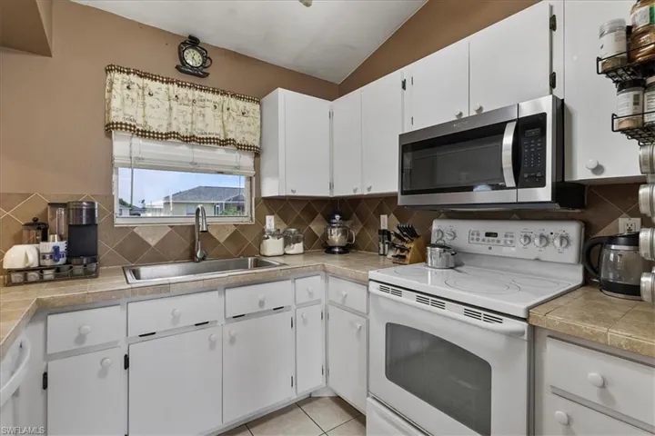 Kitchen with light tile patterned flooring, a sink, white cabinetry, tasteful backsplash, and white appliances