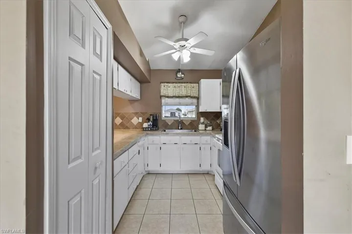 Kitchen featuring a sink, decorative backsplash, light tile patterned floors, ceiling fan, and stainless steel refrigerator with ice dispenser