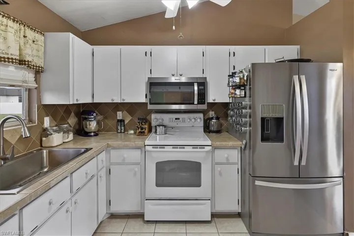 Kitchen featuring stainless steel arefrigerator, a ceiling fan, lofted ceiling, a sink, and light tile patterned floors