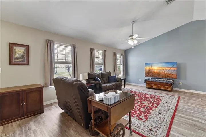 Living room with vaulted ceiling, ceiling fan, and a healthy amount of sunlight