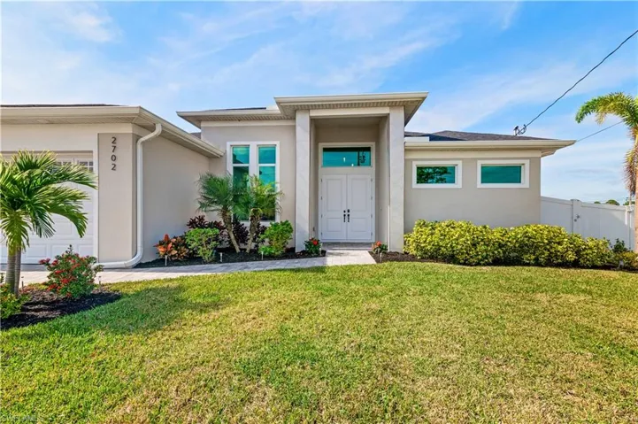 View of front of home with a garage, a front lawn, and stucco siding