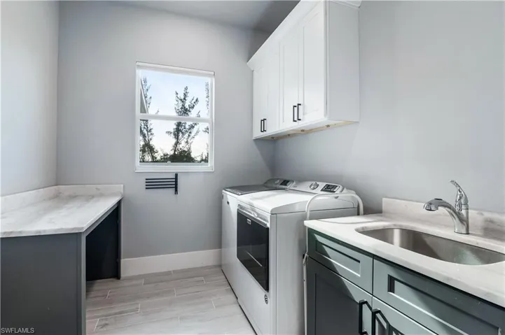 Laundry area featuring a sink, baseboards, cabinet space, wood tiled floor, and washing machine and clothes dryer