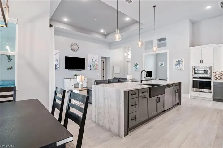 Kitchen featuring a center island with sink, stainless steel appliances, gray cabinetry, open floor plan, and a sink