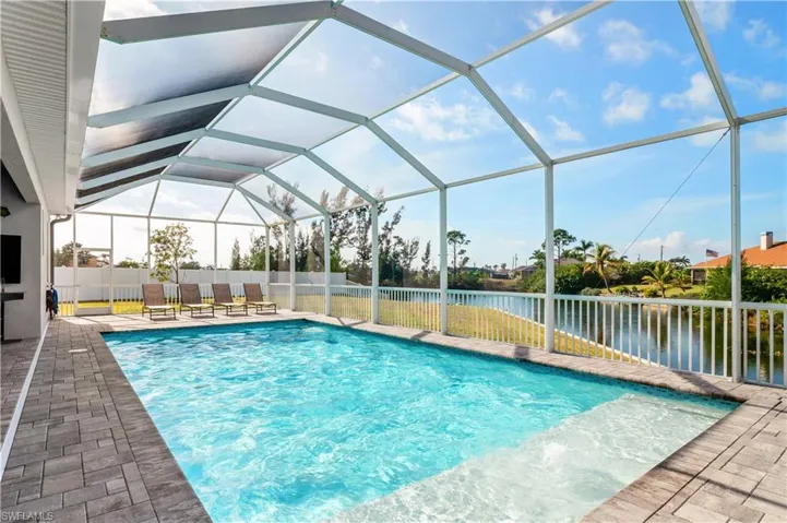 View of swimming pool with glass enclosure, a patio, a water view, and a fenced in pool