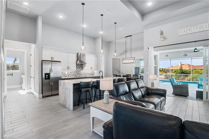 Living room featuring ceiling fan, a high ceiling, visible vents, baseboards, and light wood-style floors