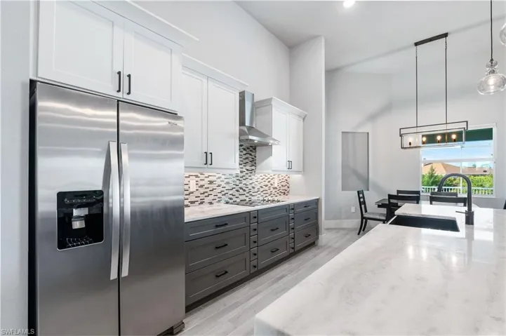 Kitchen featuring light stone counters, stainless steel refrigerator with ice dispenser, white cabinets, a sink, and wall chimney exhaust hood
