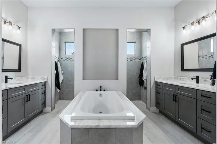 Bathroom featuring a sink, two vanities, a bath, and a walk in shower