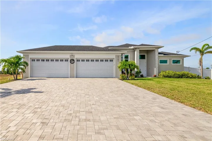 Prairie-style home with an attached garage, fence, decorative driveway, stucco siding, and a front lawn