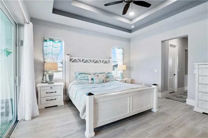 Bedroom with baseboards, a raised ceiling, a ceiling fan, and wood tiled floor