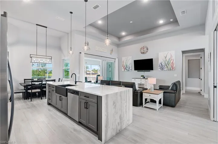 Kitchen with light stone counters, decorative light fixtures, gray cabinets, appliances with stainless steel finishes, and an island with sink