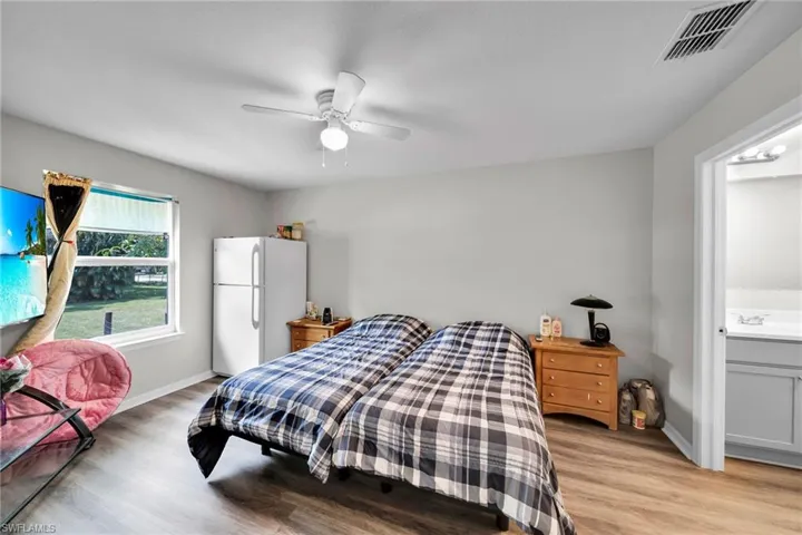 Bedroom featuring connected bathroom, white fridge, ceiling fan, and light wood-type flooring