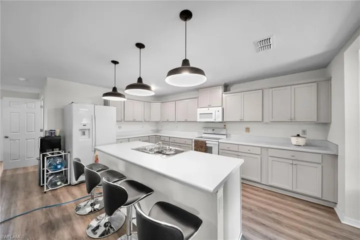 Kitchen with light hardwood / wood-style floors, a kitchen island, hanging light fixtures, a breakfast bar area, and white appliances