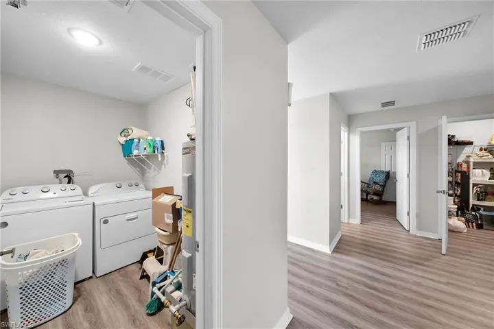 Laundry room featuring separate washer and dryer, water heater, and light hardwood / wood-style flooring