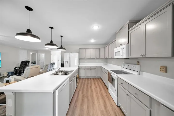 Kitchen featuring light hardwood / wood-style floors, white appliances, a center island, gray cabinetry, and sink