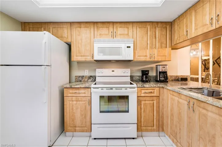 Kitchen featuring light tile patterned floors, white appliances, light stone counters, and sink