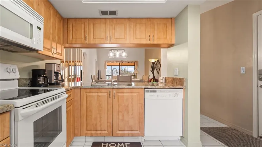 Kitchen with white appliances, an inviting chandelier, sink, light stone countertops, and light tile patterned floors