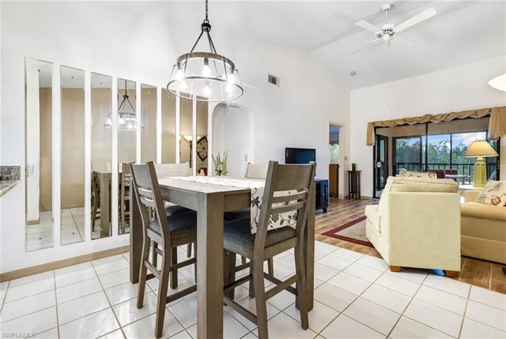 Dining area featuring ceiling fan with notable chandelier, light hardwood / wood-style floors, and vaulted ceiling