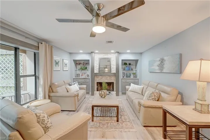 Living room with a stone fireplace, built in features, luxury vinyl plank flooring, and ceiling fan