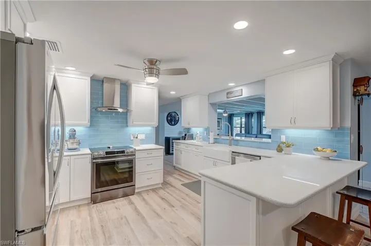 Kitchen with wall chimney range hood, appliances with stainless steel finishes, quartz countertops, a breakfast bar area, tasteful backsplash, and ceiling fan