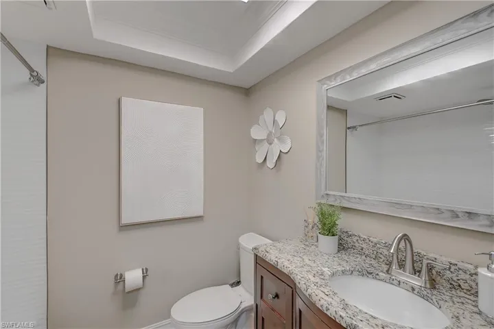 Bathroom featuring large vanity, tub, toilet, and a raised ceiling