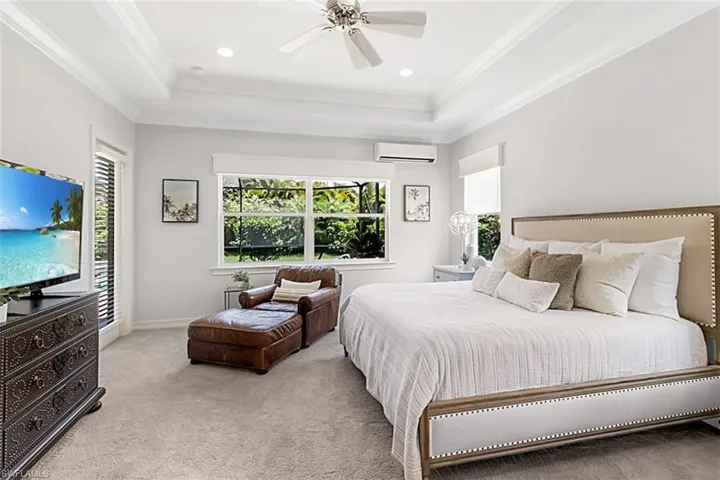 Karastan carpeted primary bedroom featuring an split AC wall unit, ceiling fan, a raised ceiling, and crown molding