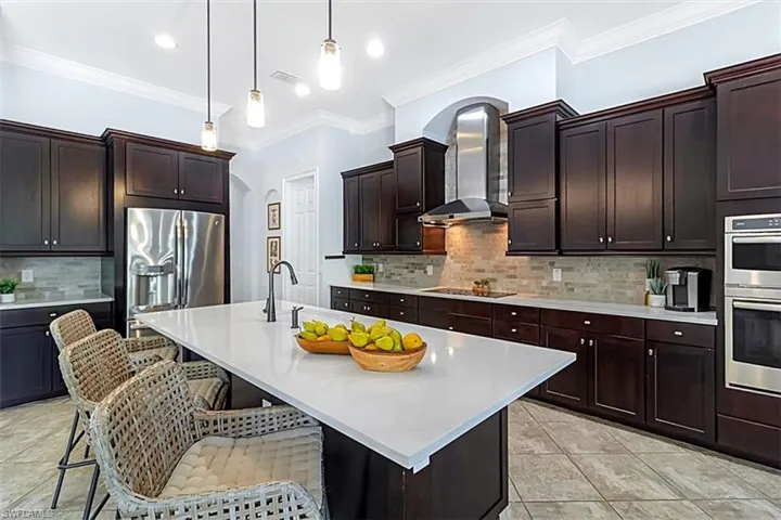 Kitchen with a quartz countertops, tile backsplash, exhaust hood, a breakfast bar area, and upscale GE appliances with stainless steel finishes
