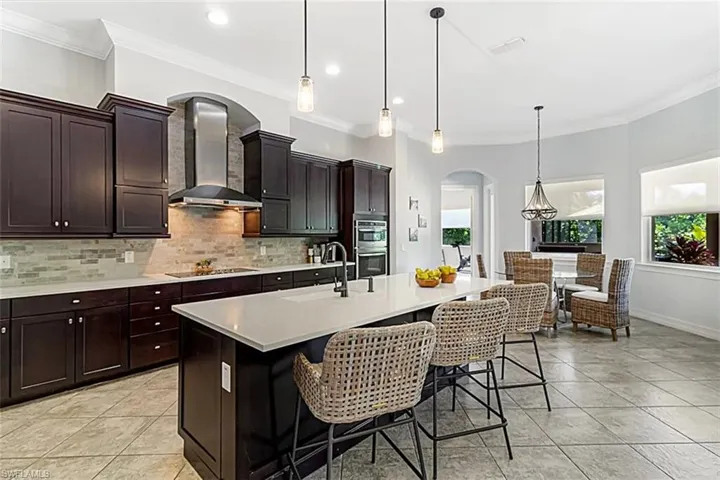 Kitchen featuring decorative pendant light fixtures, a kitchen breakfast bar, a center island with sink, exhaust hood, and stainless steel microwave & oven