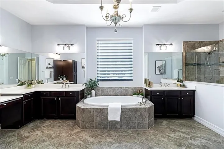 Bathroom featuring tile flooring, independent shower and soaking tub, double sink, vanity with extensive cabinet space, and a chandelier