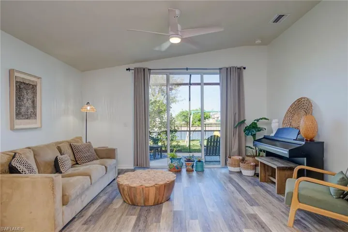 Living room featuring visible vents, ceiling fan, lofted ceiling, and light wood-style flooring