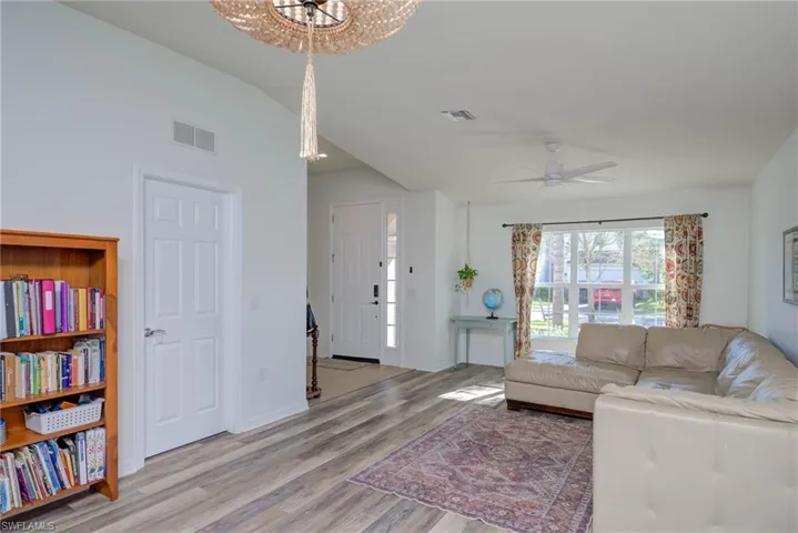 Living area with lofted ceiling, light wood-style floors, baseboards, and visible vents