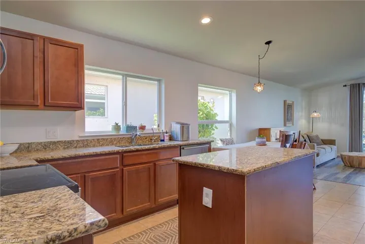 Kitchen featuring light stone counters, pendant lighting, a kitchen island, and a sink