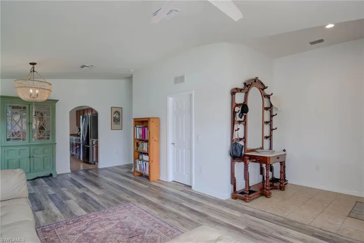 Living room featuring light wood-type flooring, lofted ceiling, visible vents, and arched walkways