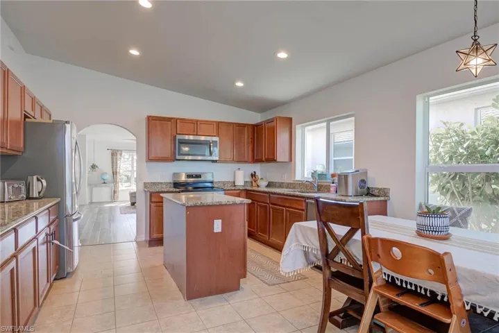 Kitchen featuring arched walkways, a kitchen island, decorative light fixtures, light stone countertops, and stainless steel appliances